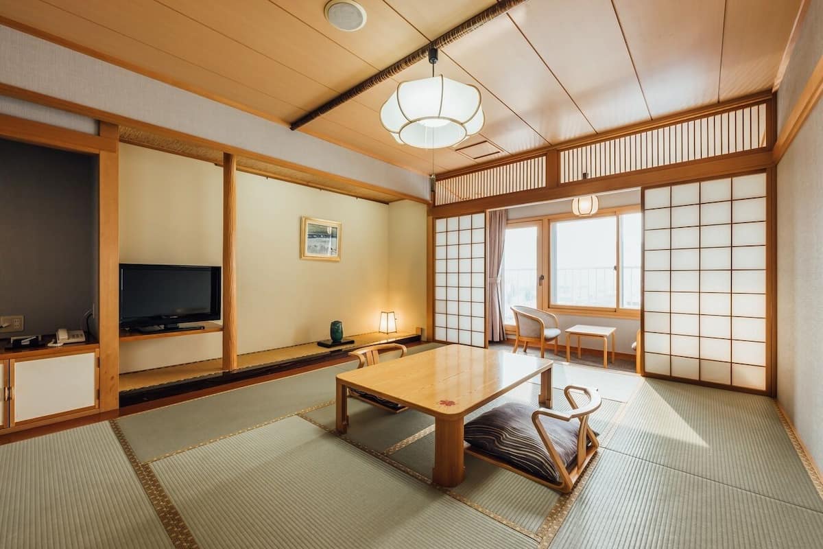 A traditional Japanese room with tatami flooring, a low table, a television, and sliding doors.