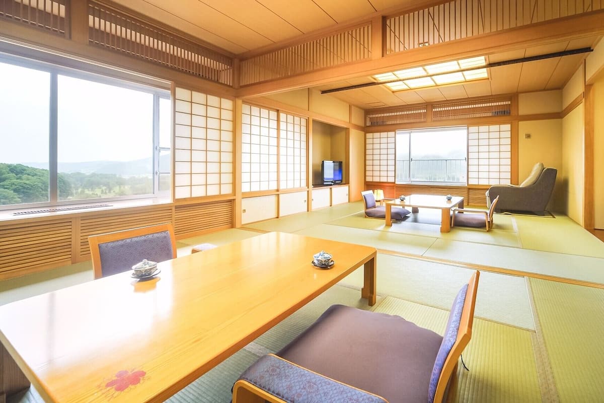 A traditional Japanese room with tatami flooring, a low table, seating, and a television.