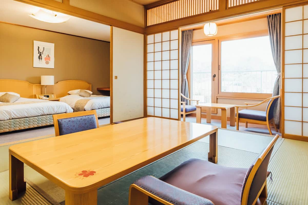 A traditional Japanese-style room with tatami flooring, a low table with cushions, a bed with a headboard, and a sliding shoji screen.