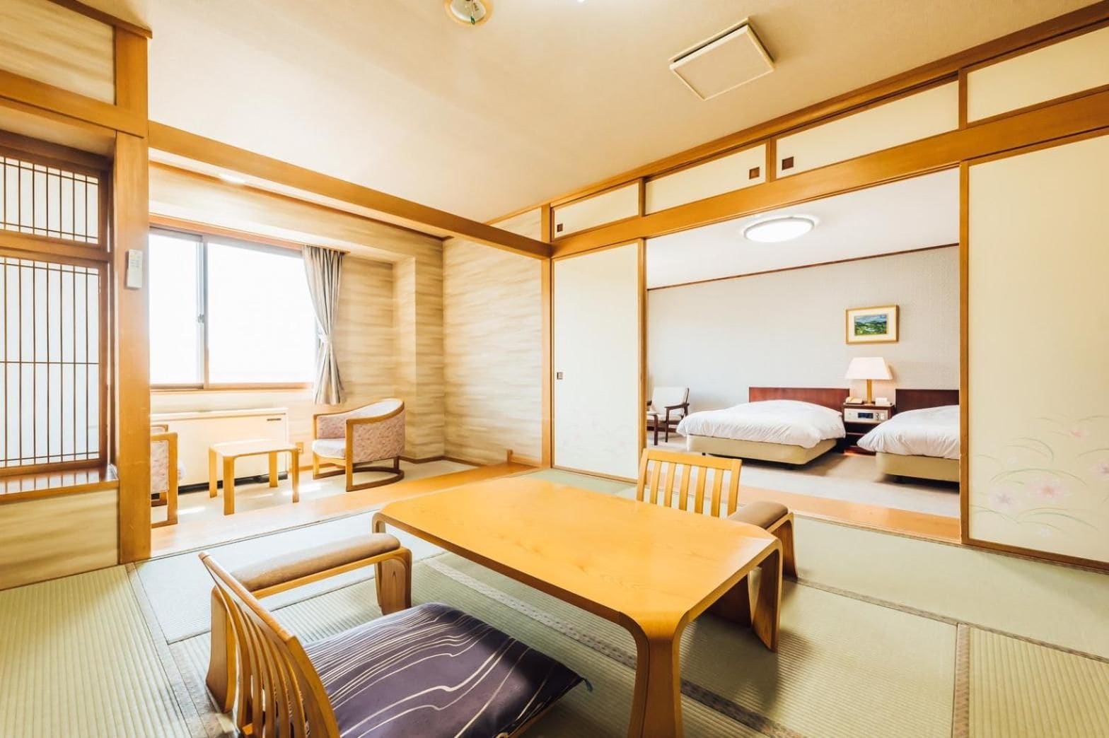 A traditional Japanese-style room with tatami flooring, a low table with chairs, a bed, and sliding doors.