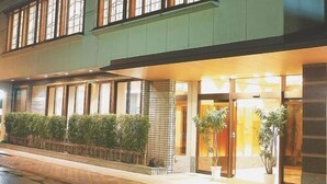 A hotel with a green facade, multiple windows, and a well-lit entrance with potted plants. - Hotel Tsuruya (Mitsuke)