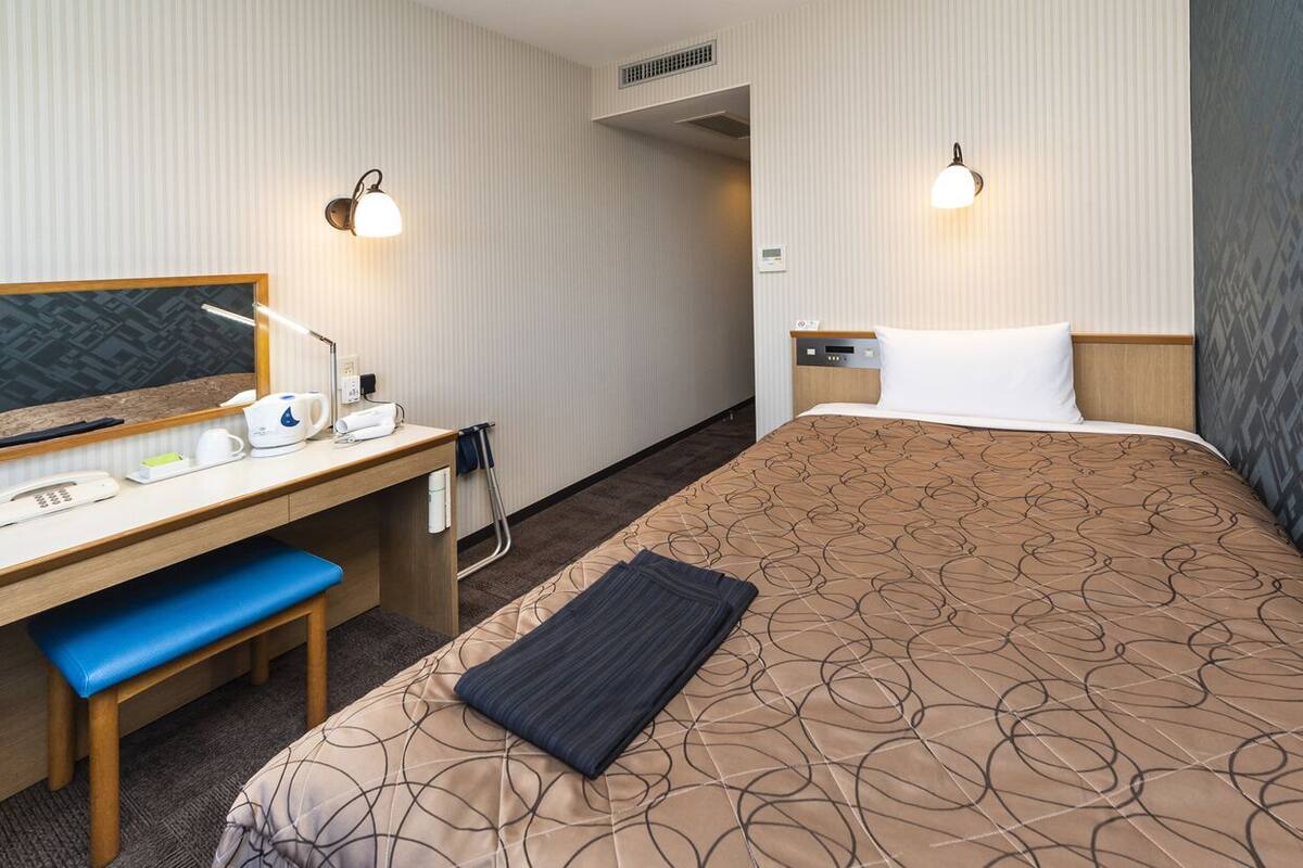 A hotel room with a bed, desk, chair, and bedside table.