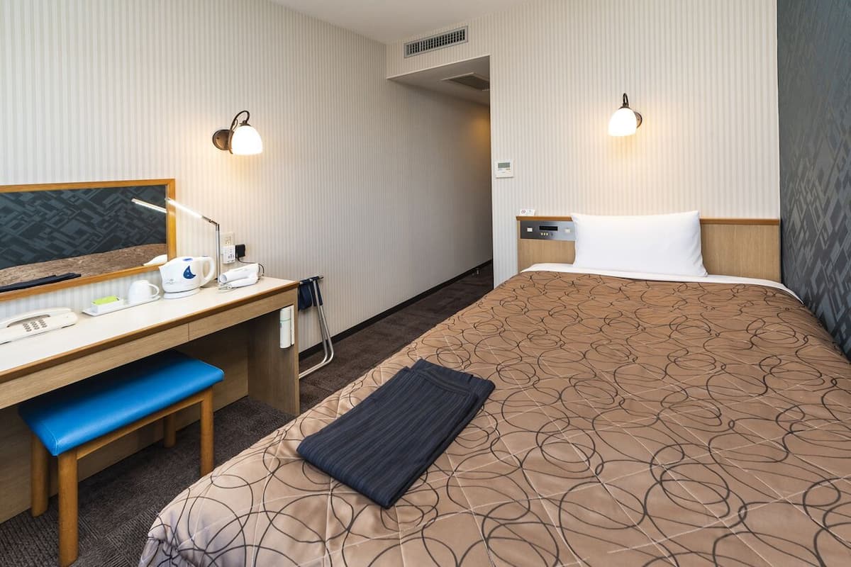 A hotel room with a bed, desk, chair, and bedside table.