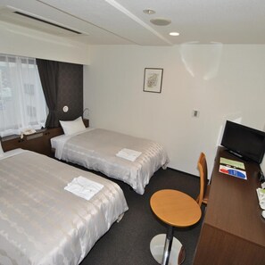 A hotel room with two beds, a desk with a chair, a television, and a window with curtains.