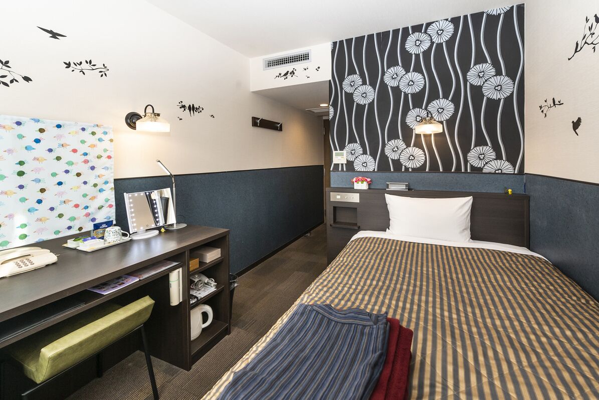 A hotel room with a bed, desk, and a wall with a floral pattern.