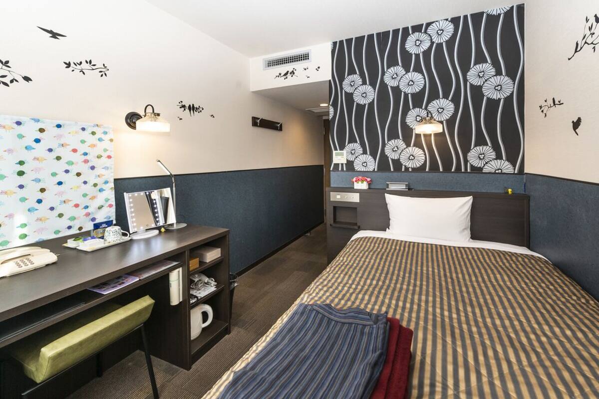 A hotel room with a bed, desk, and a wall with a floral pattern.