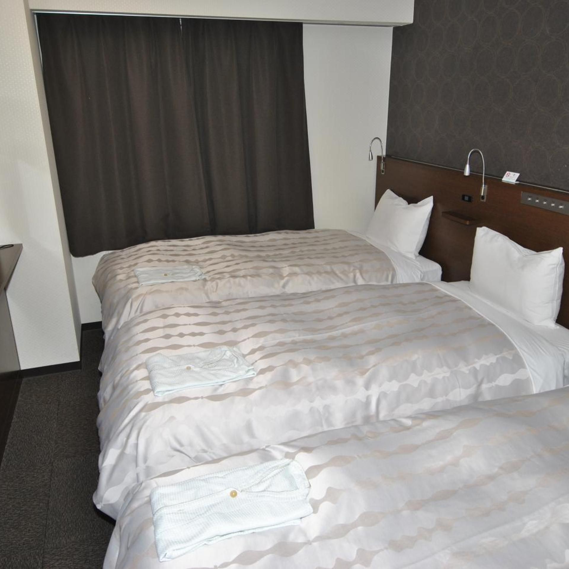 A hotel room with two beds, a headboard, a curtain, and a small table.