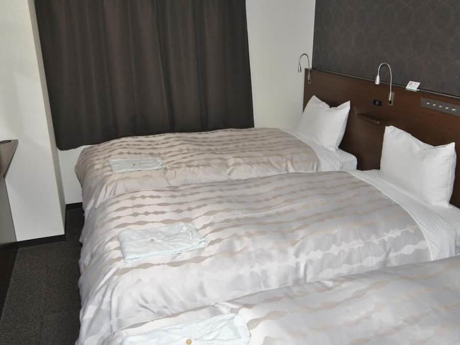 Una habitación de hotel con dos camas, un cabecero, una cortina y una mesita.