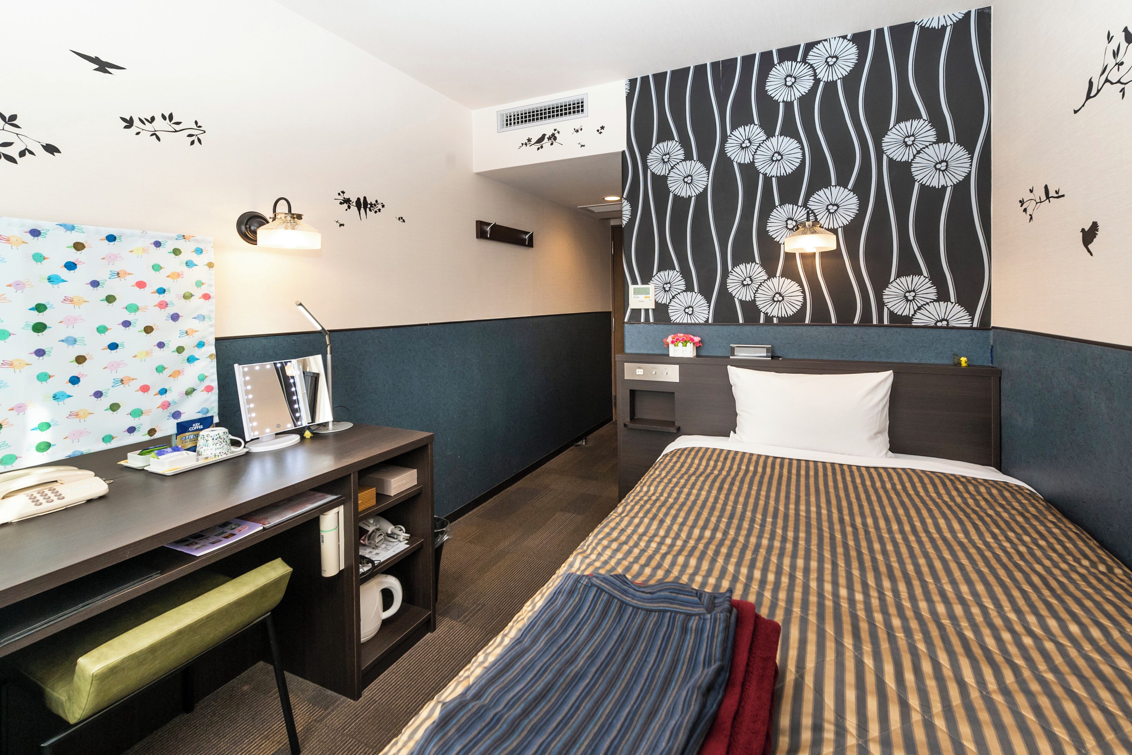 A hotel room with a bed, desk, chair, and a large wall decoration.