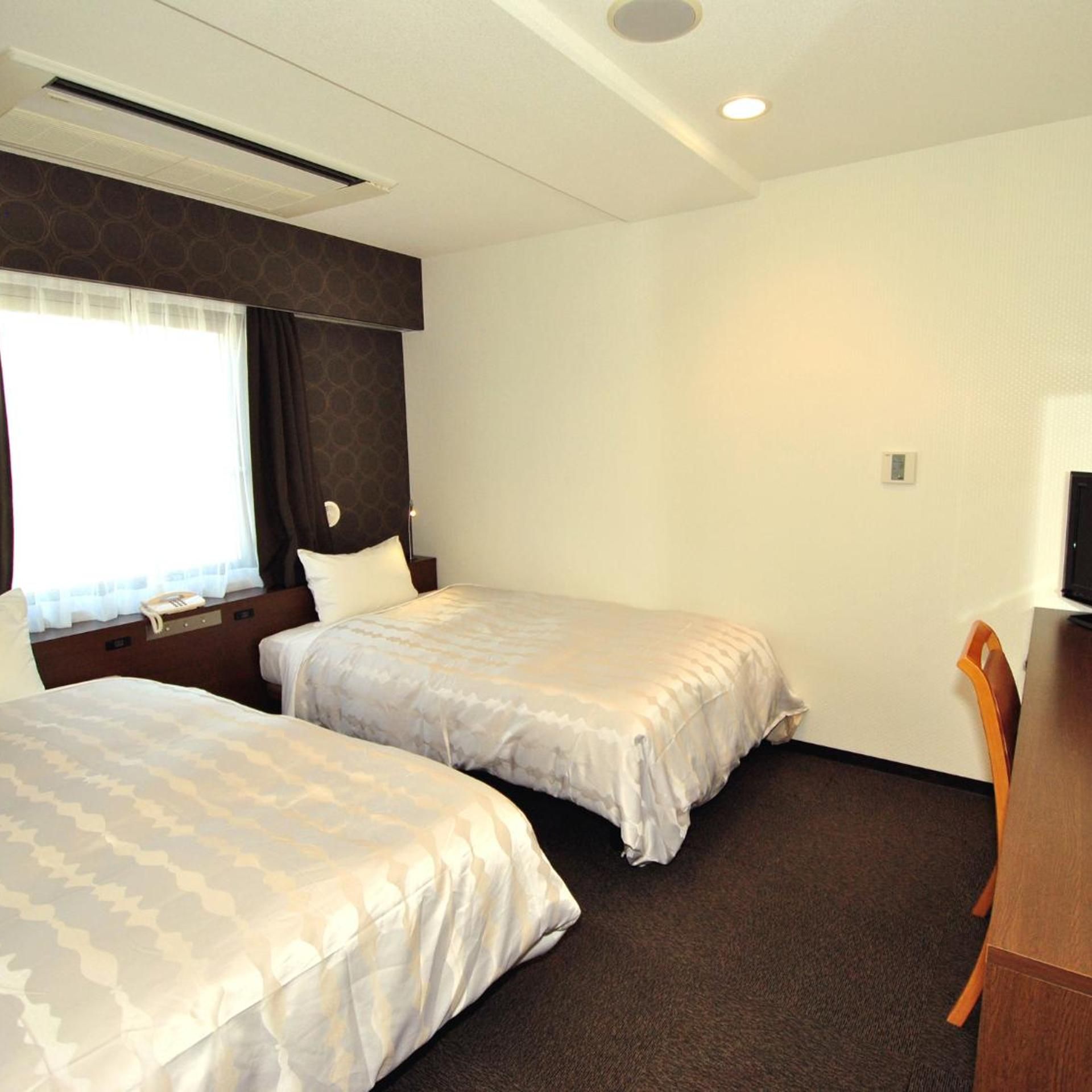 Quarto de hotel com duas camas, uma escrivaninha e uma cadeira.