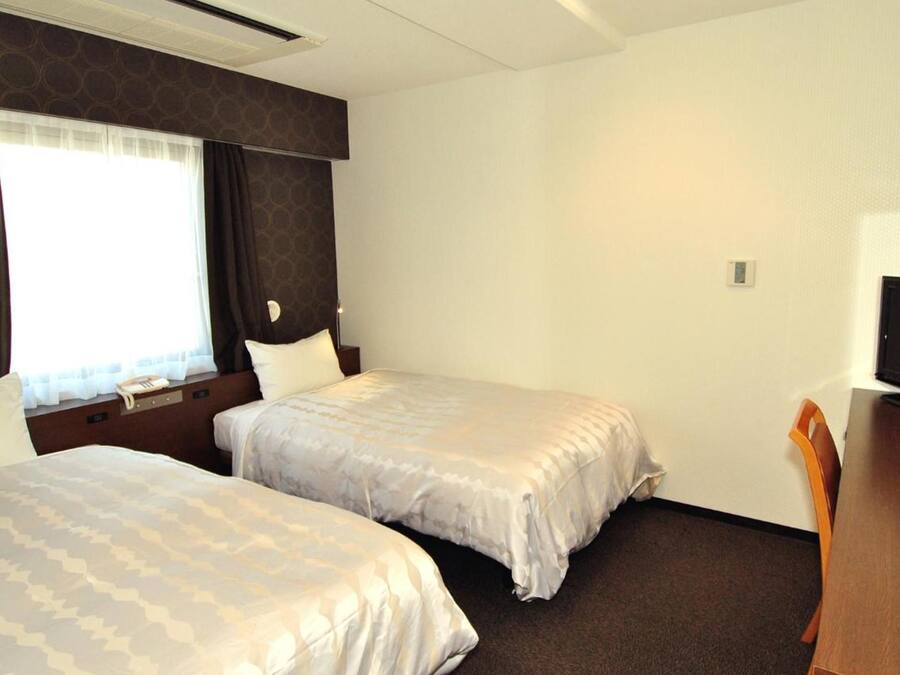 Quarto de hotel com duas camas, uma escrivaninha e uma cadeira.