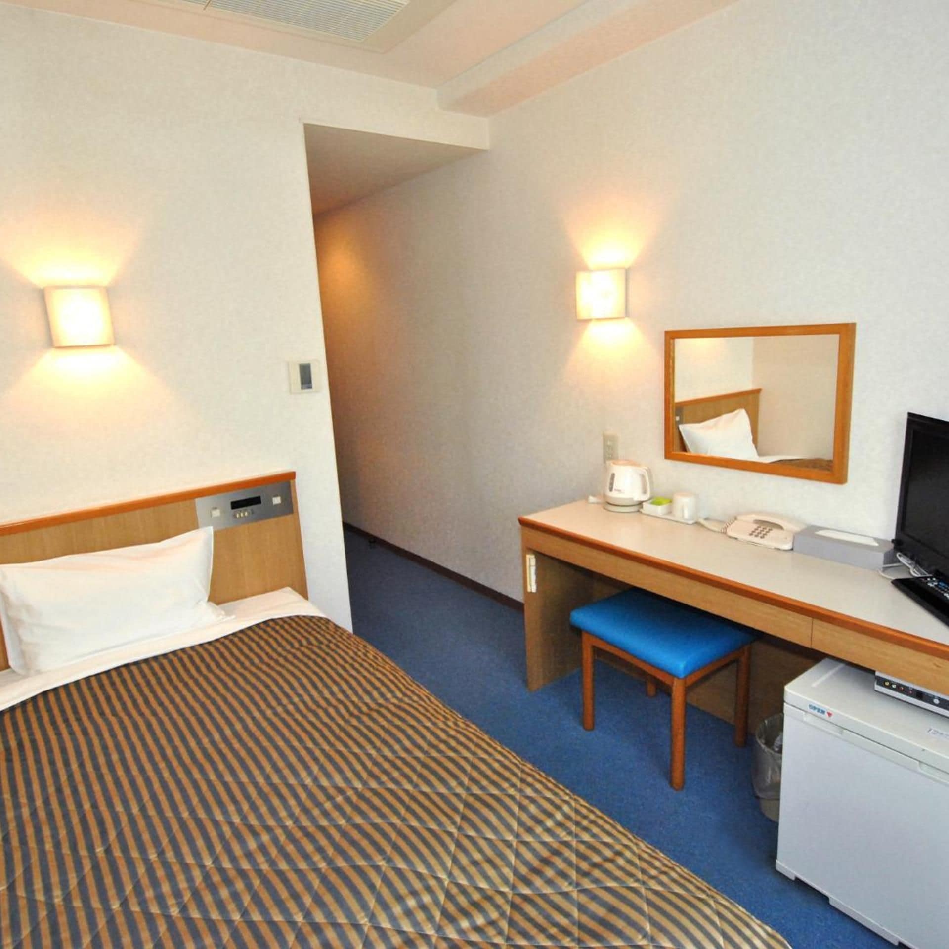 A hotel room with a bed, a desk with a chair, a television, and a small refrigerator.