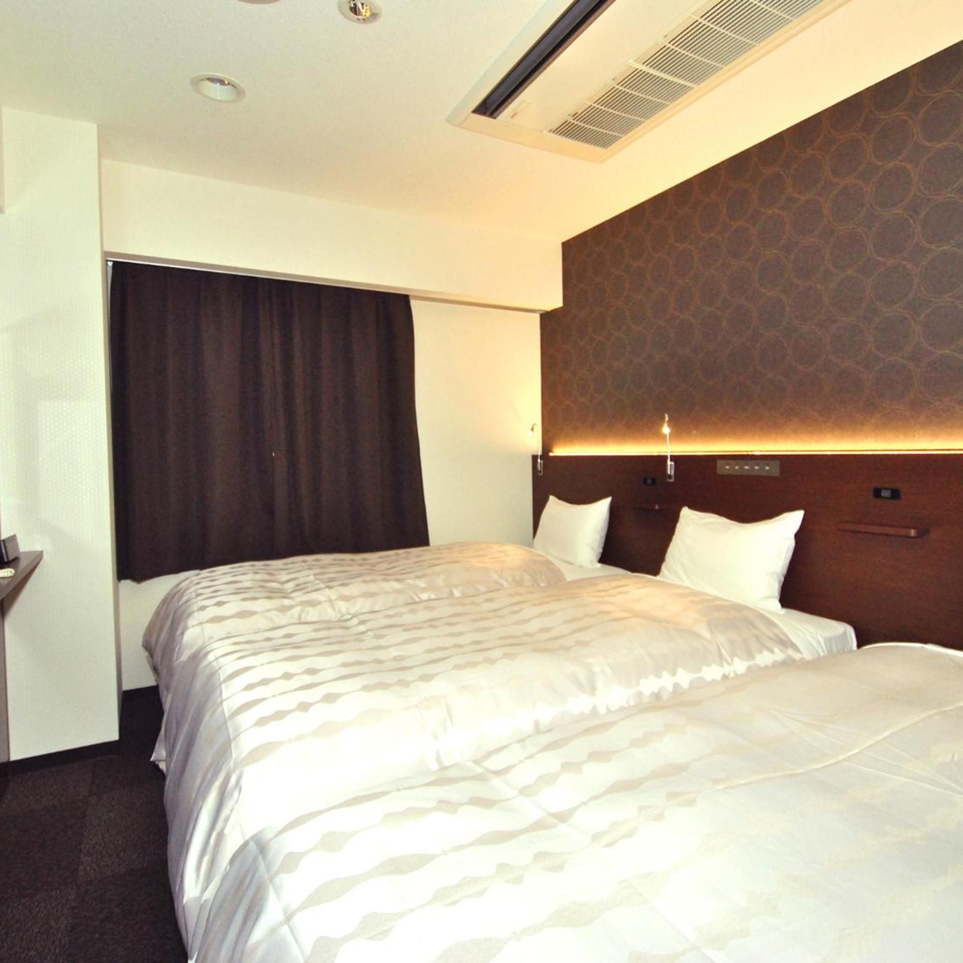 A hotel room with a large bed, a headboard with a patterned design, a bedside table, and a window with curtains.