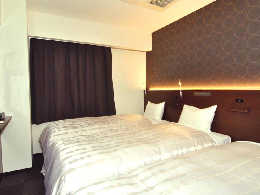 A hotel room with a large bed, a headboard with a patterned design, a bedside table, and a window with curtains.