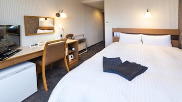 A hotel room with a bed, desk, chair, and a small refrigerator.