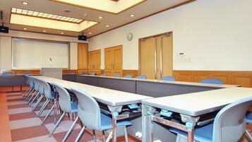 Sala de conferências com uma mesa comprida, cadeiras, tela de projetor e um relógio na parede.
