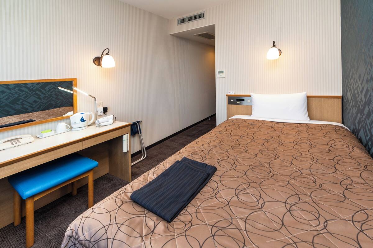 A hotel room with a bed, desk, chair, and two wall-mounted lamps.