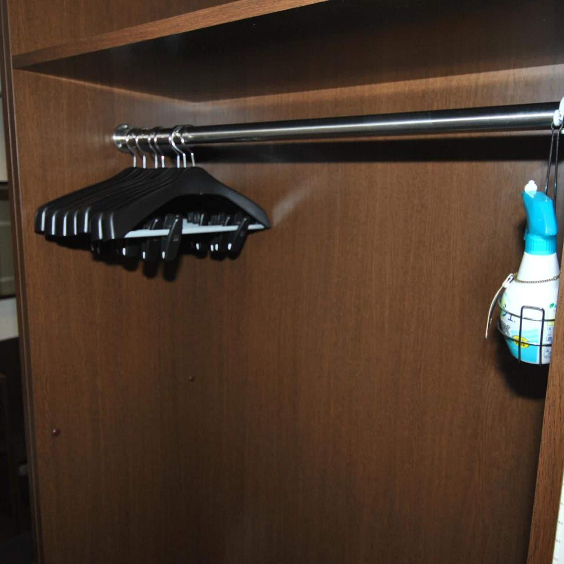 A wooden closet with a black hanger and a white bottle with a blue cap.