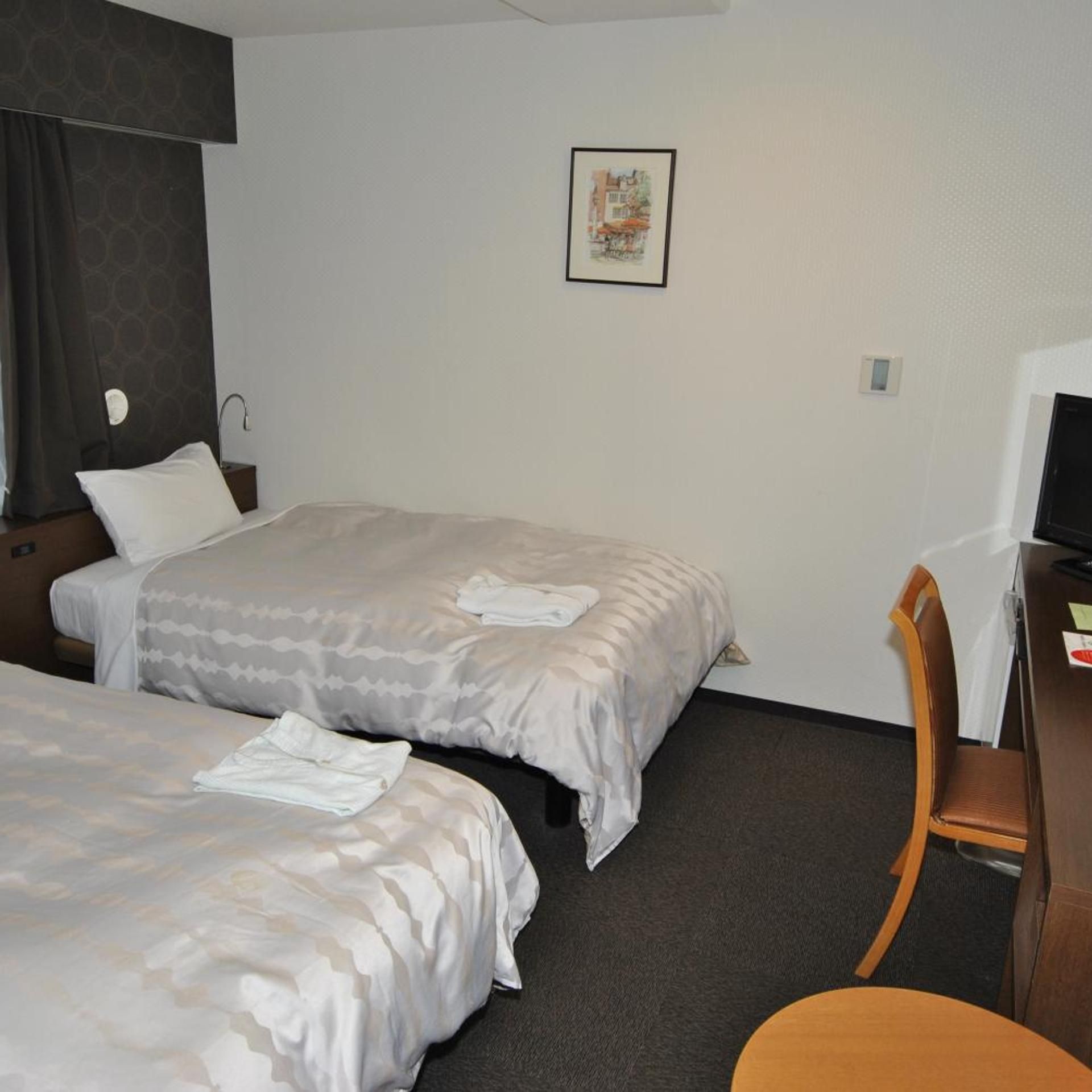 A hotel room with two beds, a desk, a chair, and a wall-mounted television.
