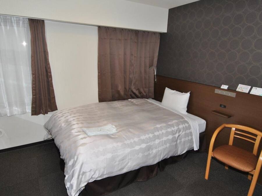 Habitación de hotel con cama, una silla de madera, una ventana con cortinas y una pared con un diseño circular.