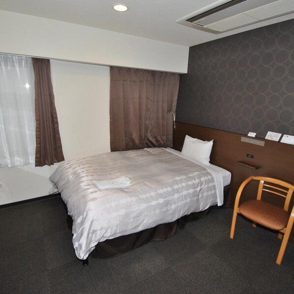 Habitación de hotel con cama, una silla de madera, una ventana con cortinas y una pared con un diseño circular.