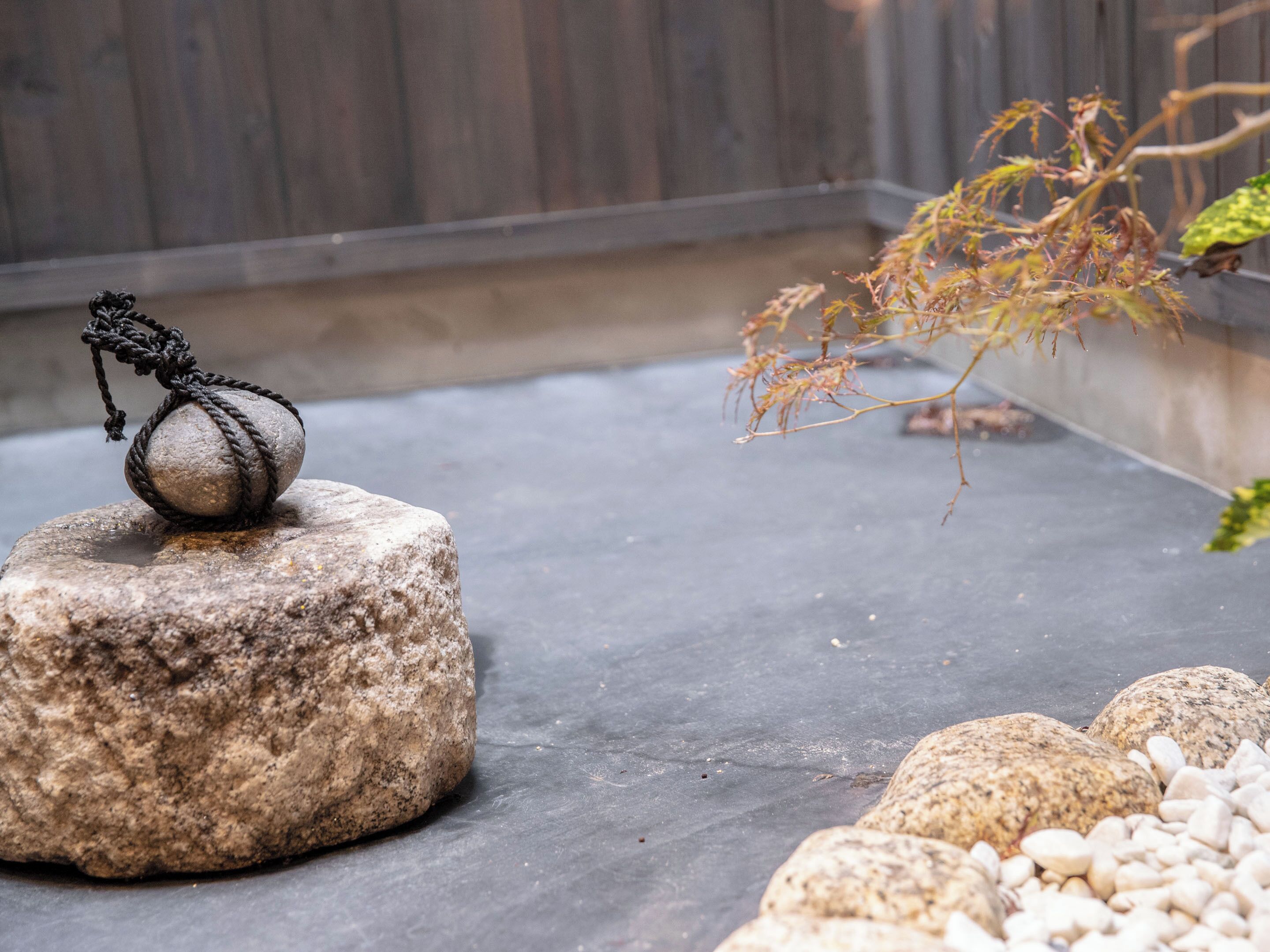 A stone with a rope tied around it, placed on a concrete surface with a wooden fence in the background.