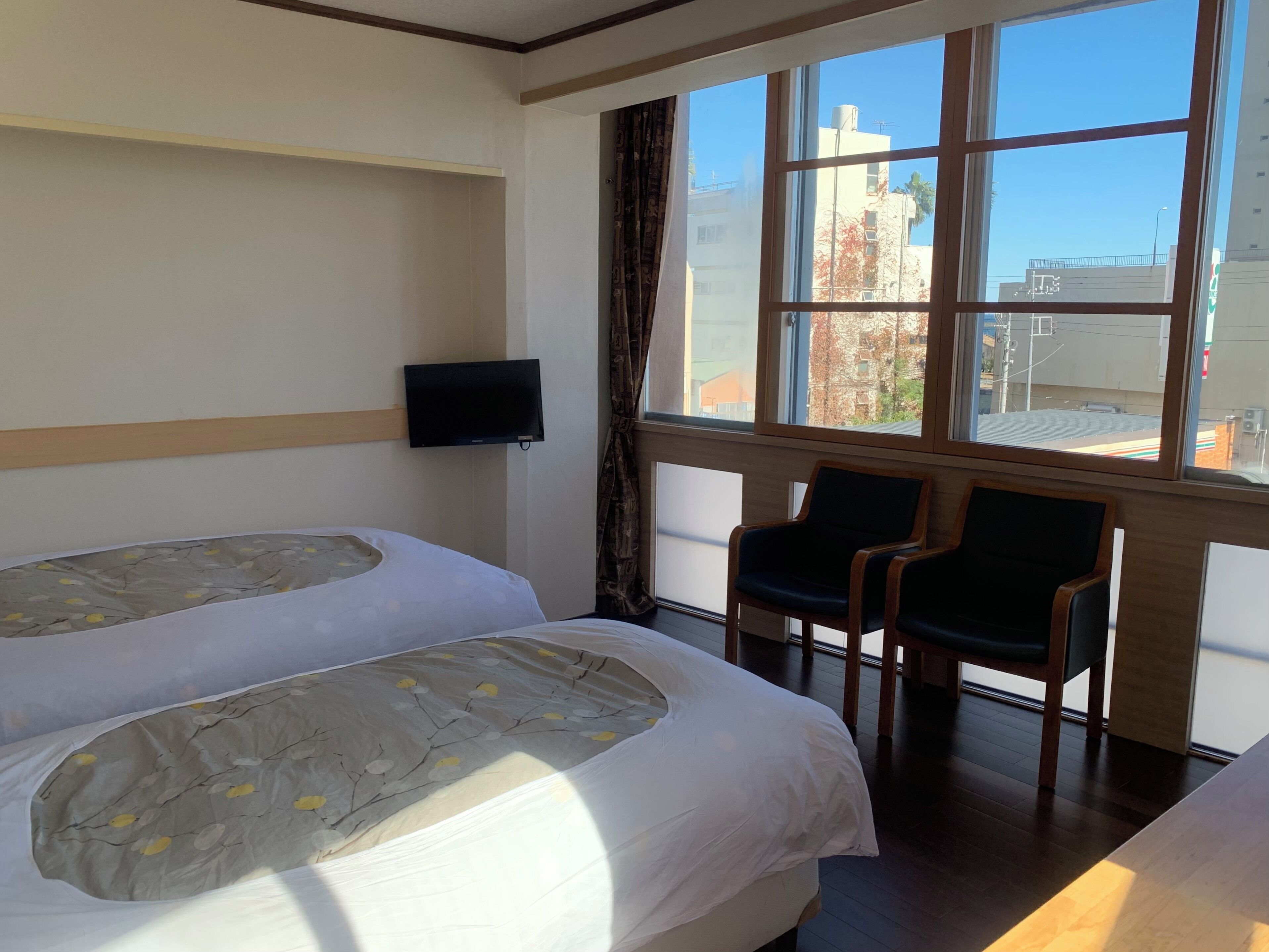 A hotel room with two beds, a TV, and a window with a view of buildings.