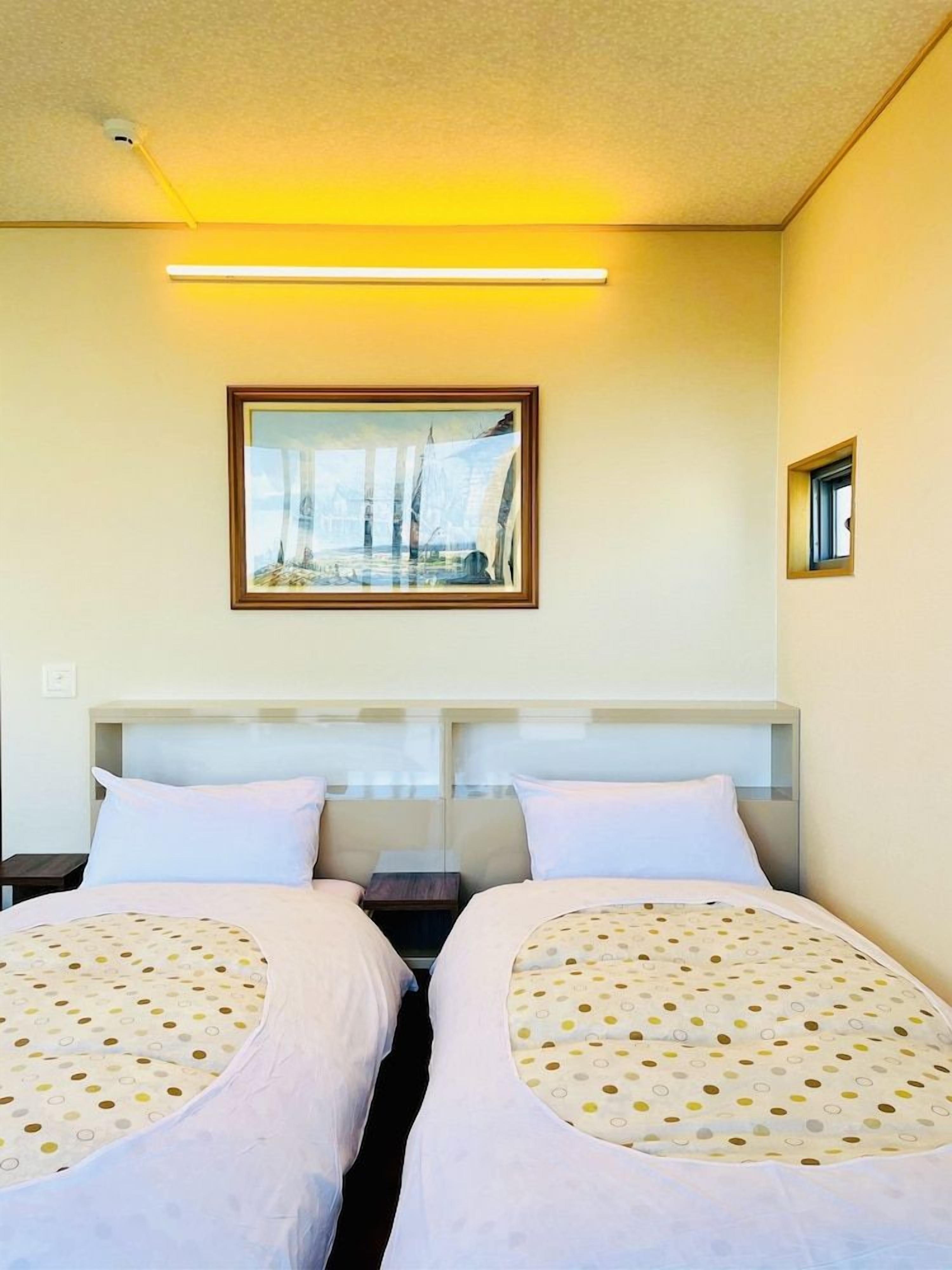 A hotel room with two beds, a framed picture on the wall, and a small window.
