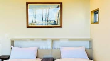A hotel room with two beds, a framed picture on the wall, and a small window.