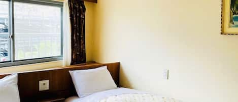 A room with two beds, a window with curtains, an air conditioning unit, and a framed picture on the wall.
