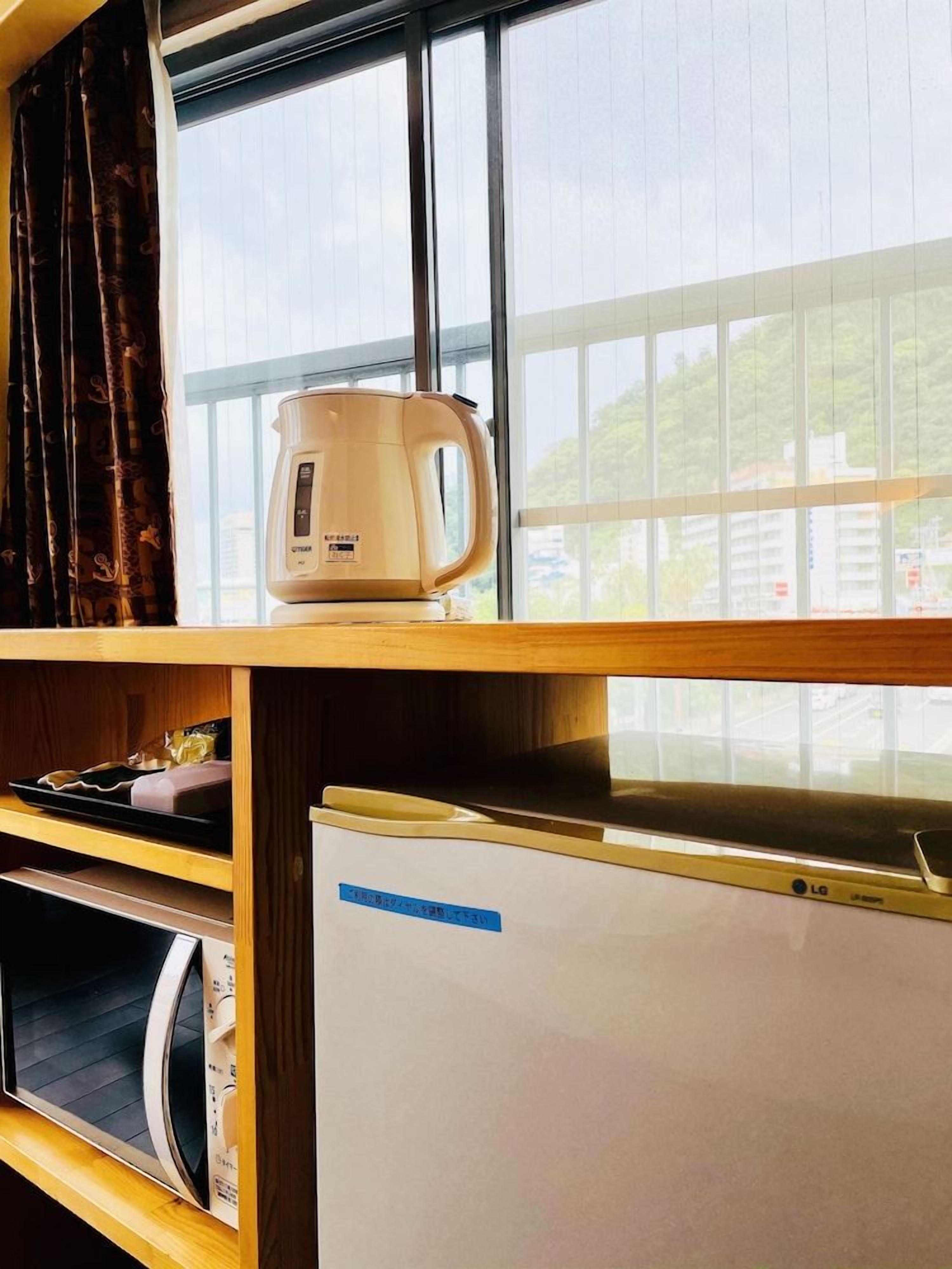 A room with a coffee maker on a shelf, a whiteboard, and a window with a view of buildings and greenery.