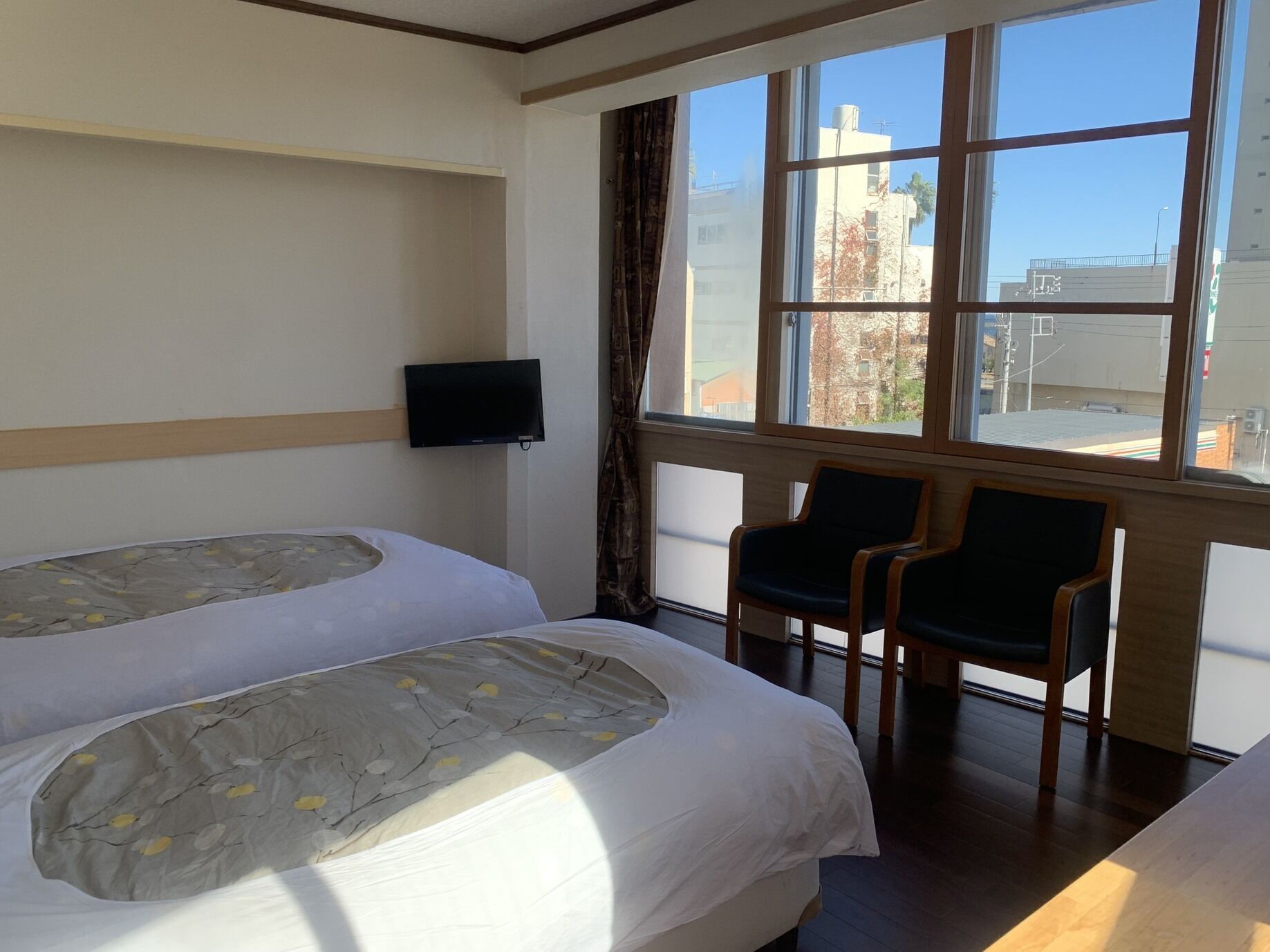 A hotel room with two beds, a TV, a window with a city view, and two chairs.