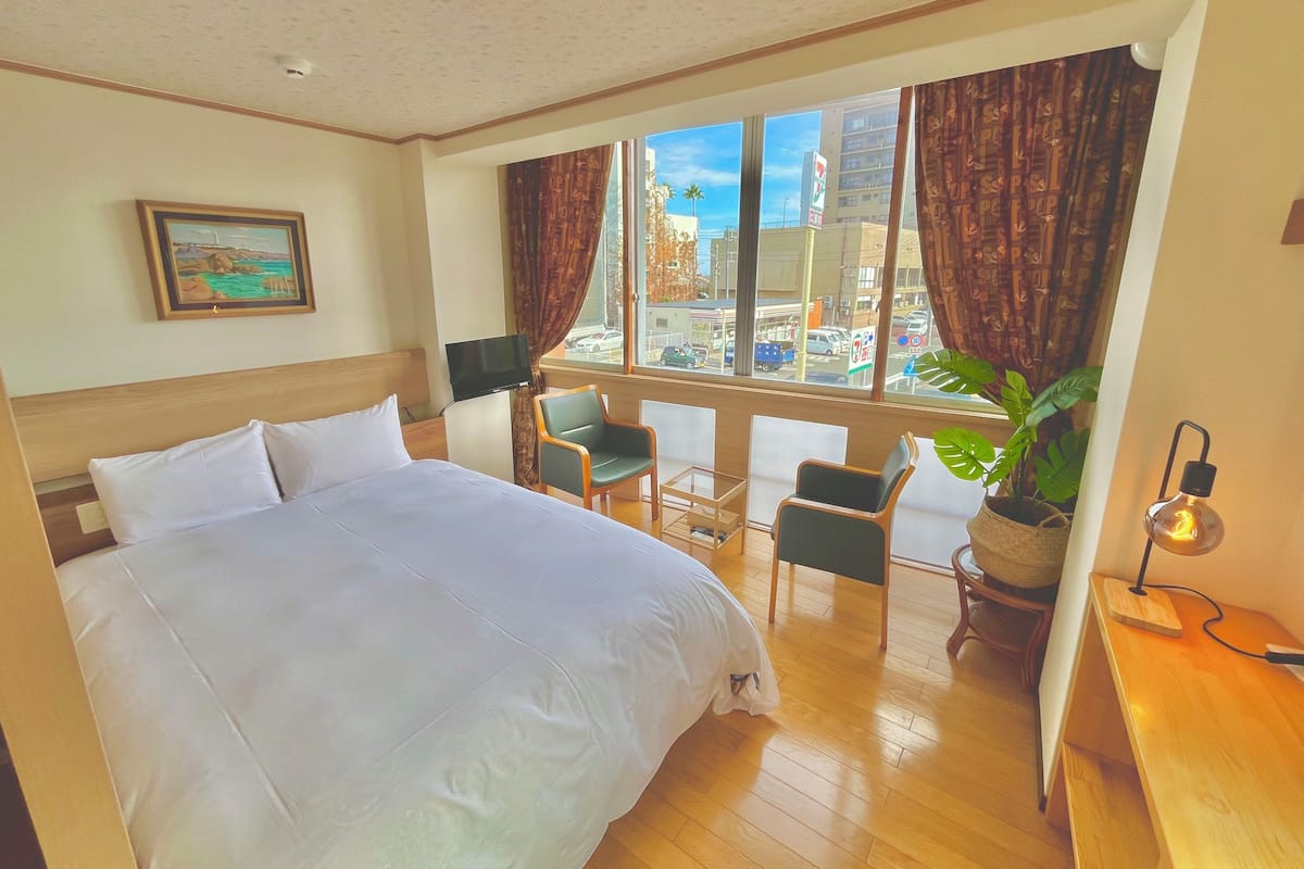 A hotel room with a bed, a desk, a chair, a TV, and a view of the city.