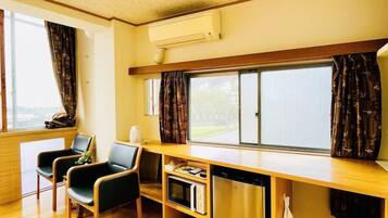 A room with a wooden floor, a desk with a chair, a window with curtains, and an air conditioning unit.