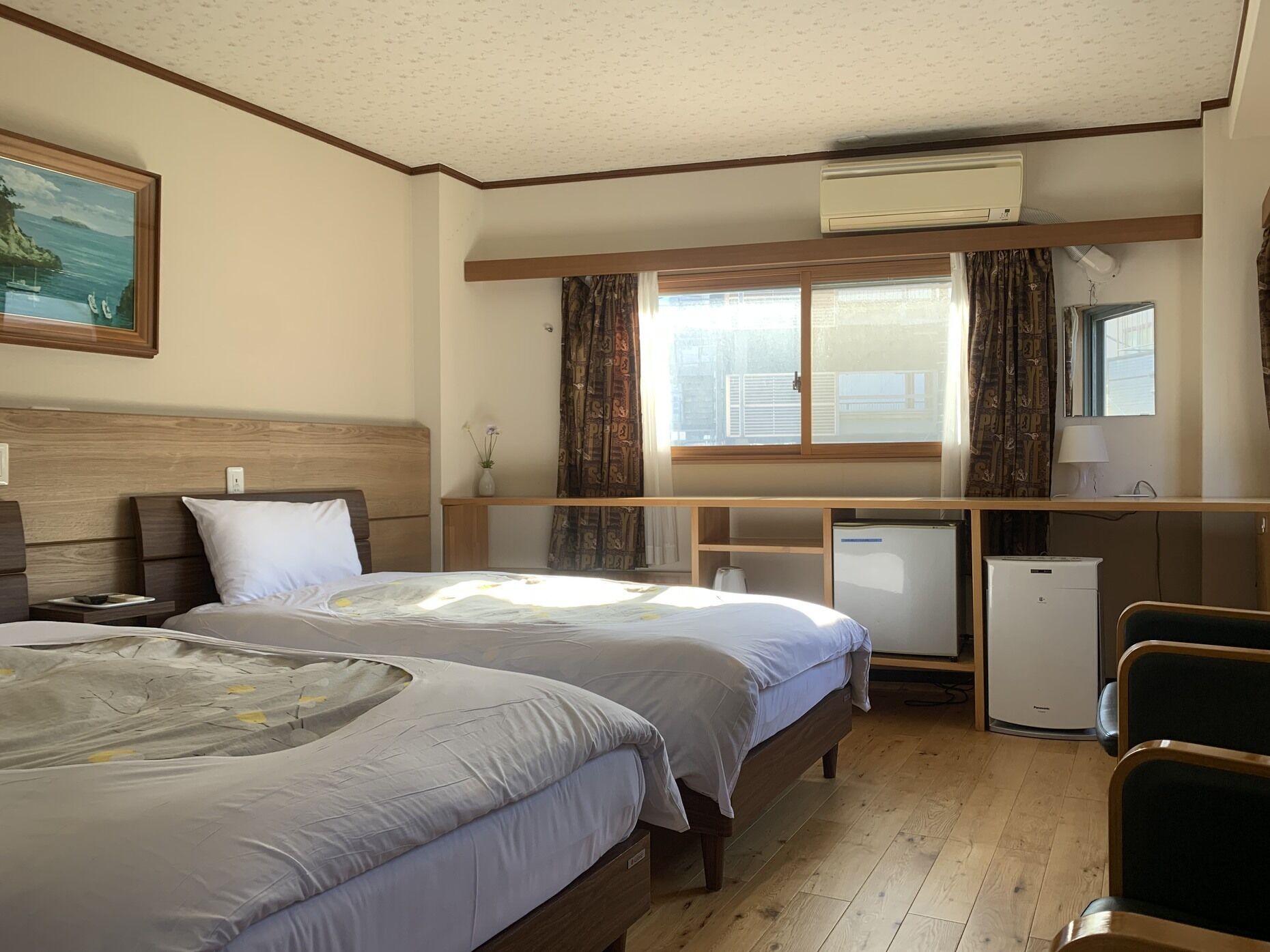 A hotel room with two beds, a desk, a refrigerator, and a window with curtains.