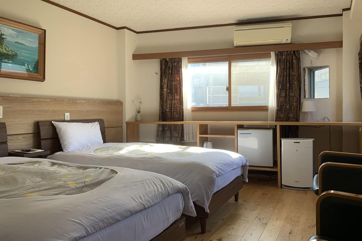 A hotel room with two beds, a desk, a refrigerator, and a window with curtains.