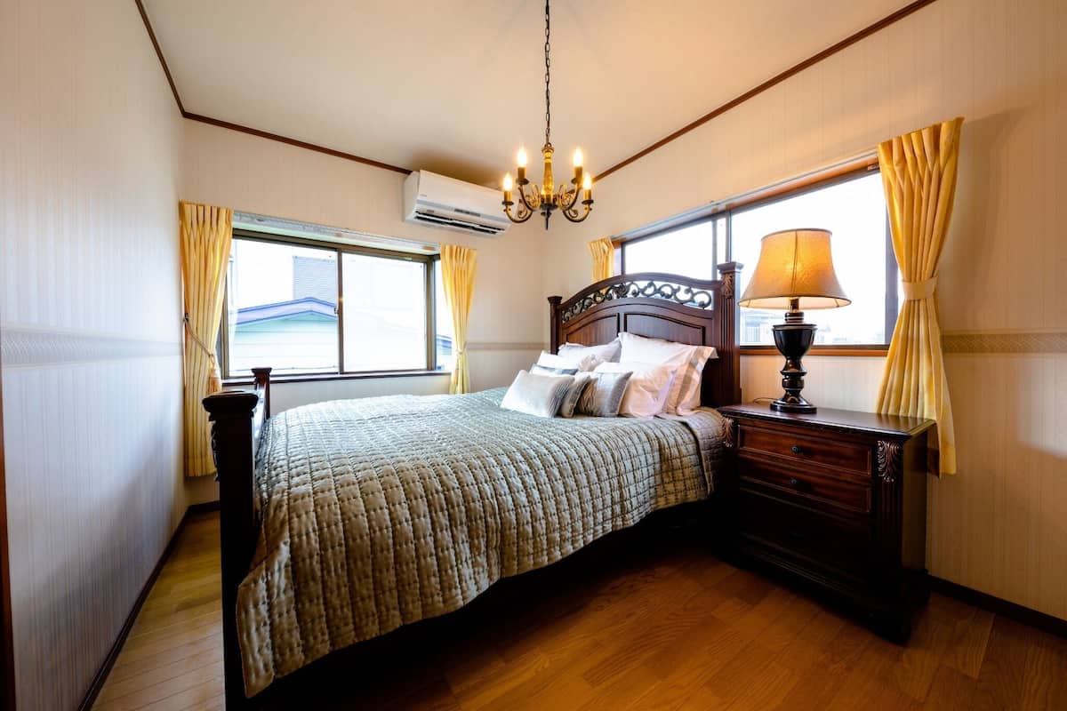 Une chambre à coucher avec un lit, une table de chevet, une lampe et une fenêtre avec des rideaux.