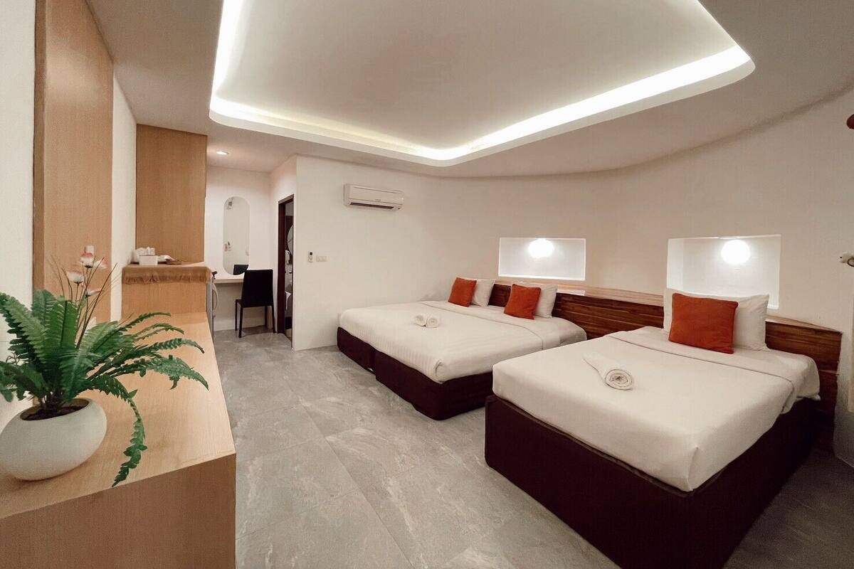 A hotel room with two beds, a desk, and a potted plant.