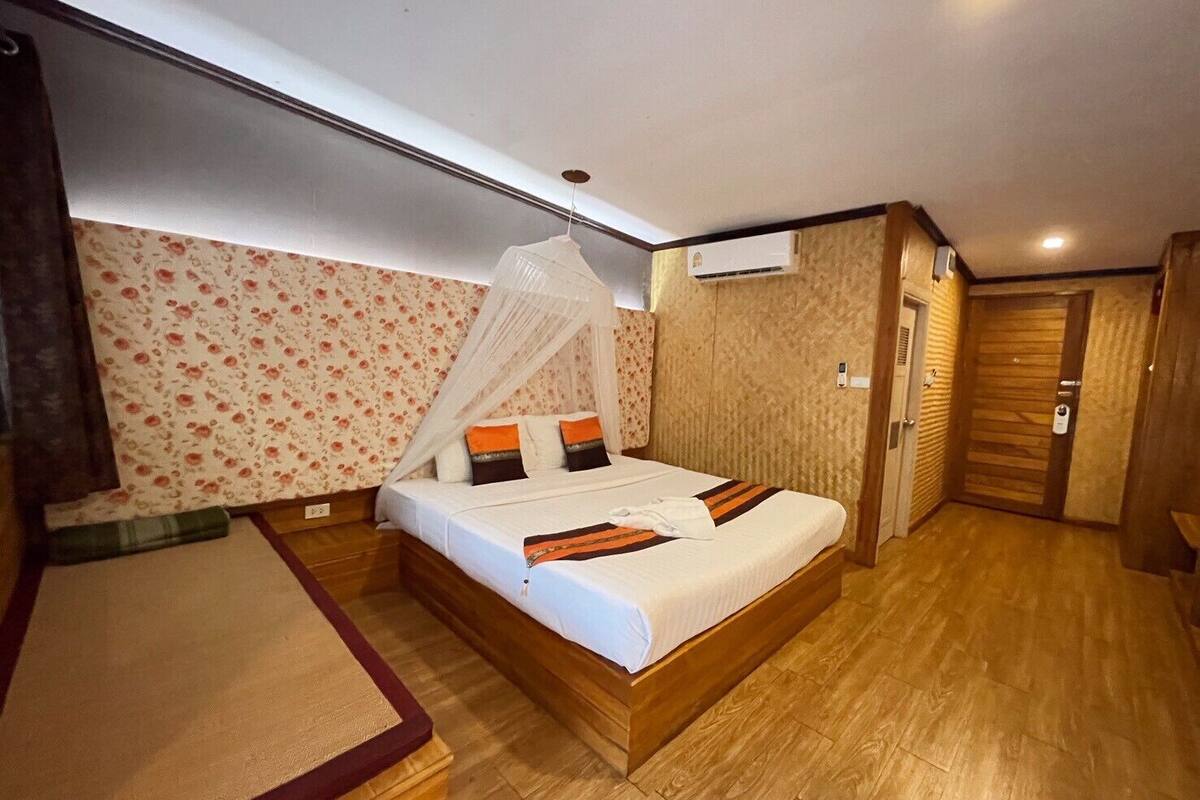 A bedroom with a wooden bed, a canopy, floral wallpaper, and a wooden floor.