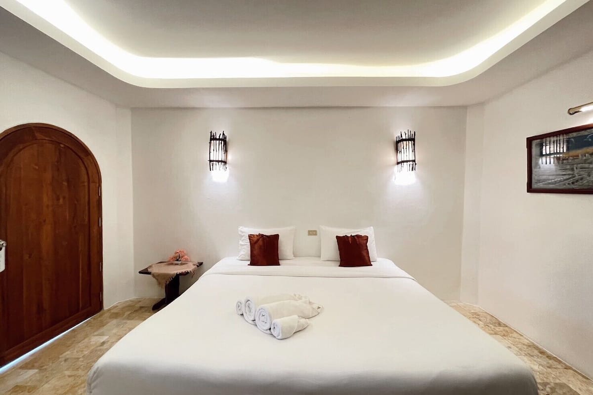 A hotel room with a large bed, two wall-mounted lights, a wooden door, and a small table with a vase.
