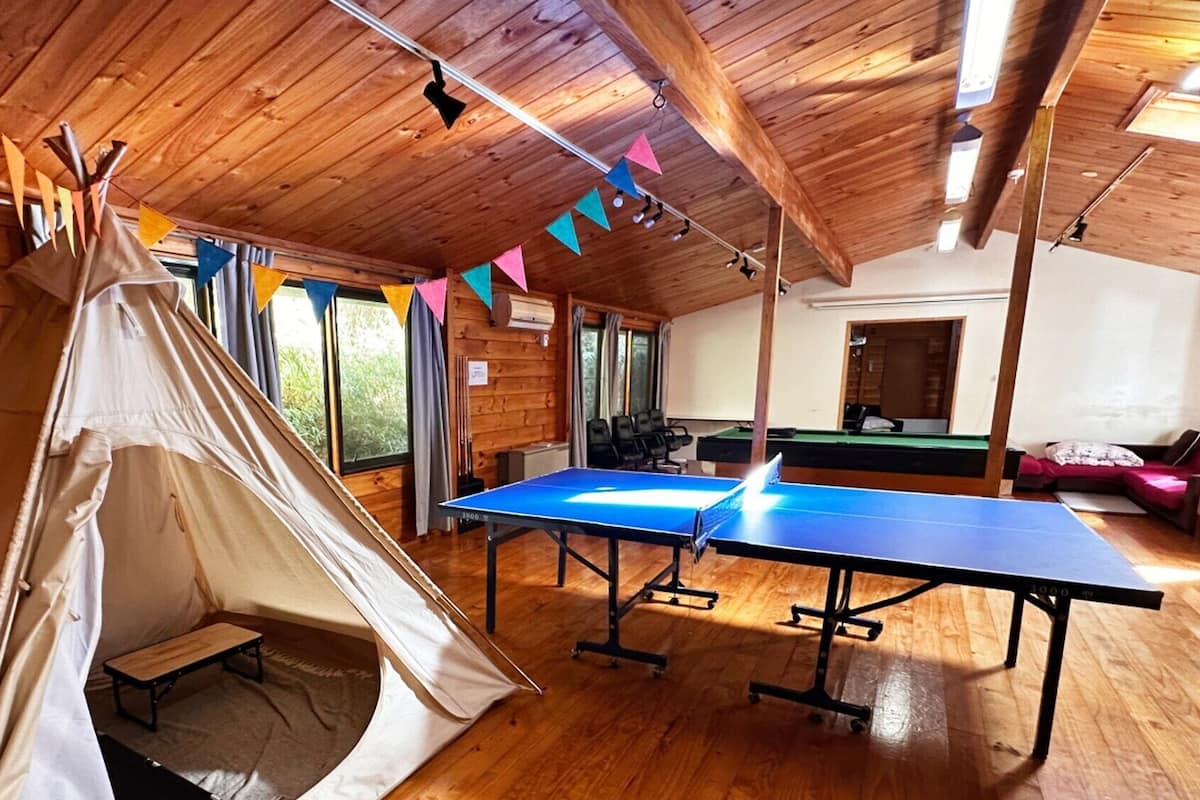 Una tienda de campaña, una mesa de ping pong y una mesa de billar en una habitación de madera con ventanas amplias.