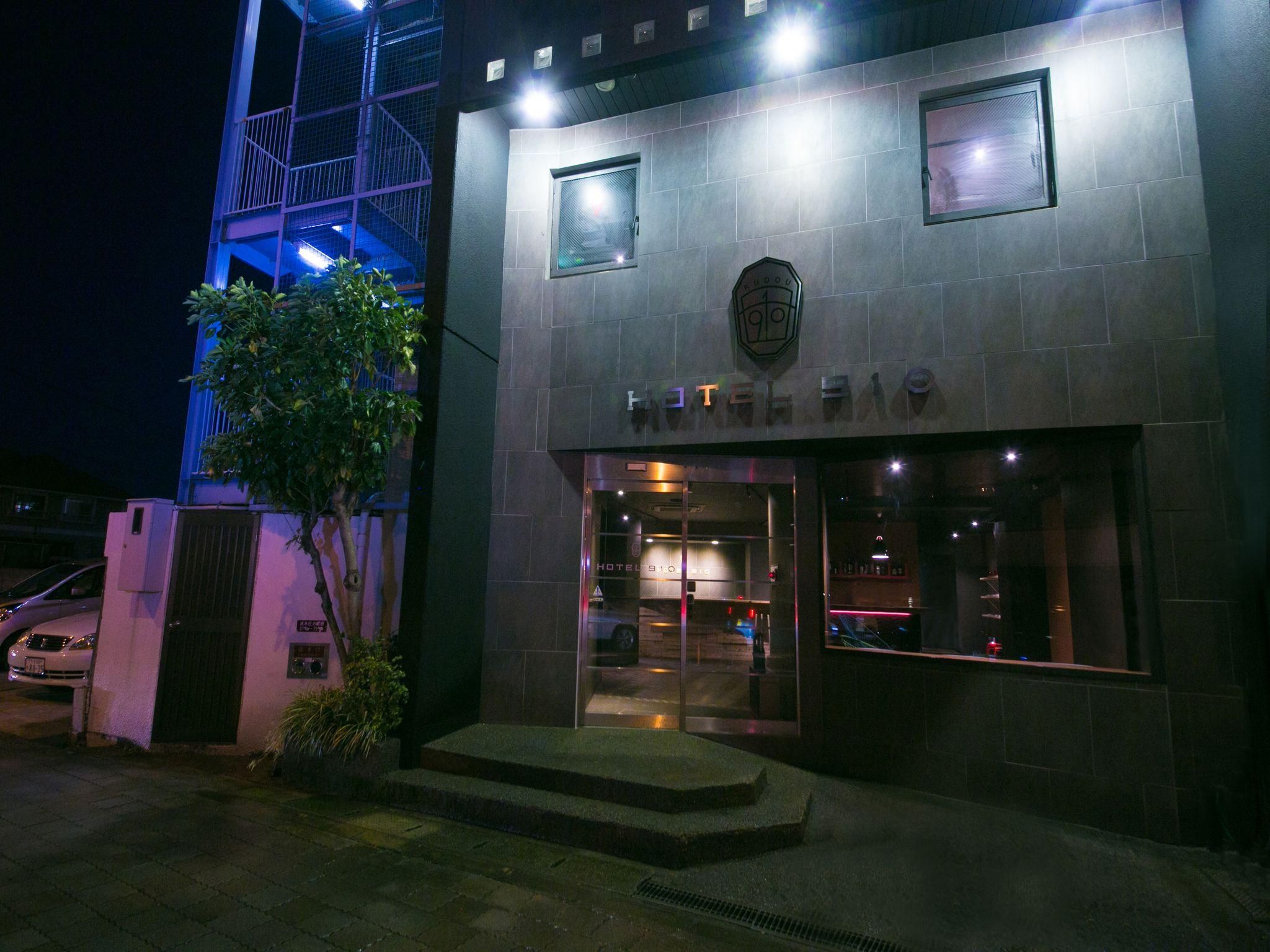 A hotel entrance with a modern facade, a visible staircase leading to the entrance, and a car parked outside.