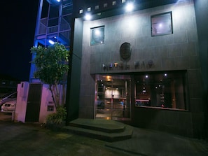 A hotel entrance with a modern facade, a visible staircase leading to the entrance, and a car parked outside. - Hotel 910 (Oita)