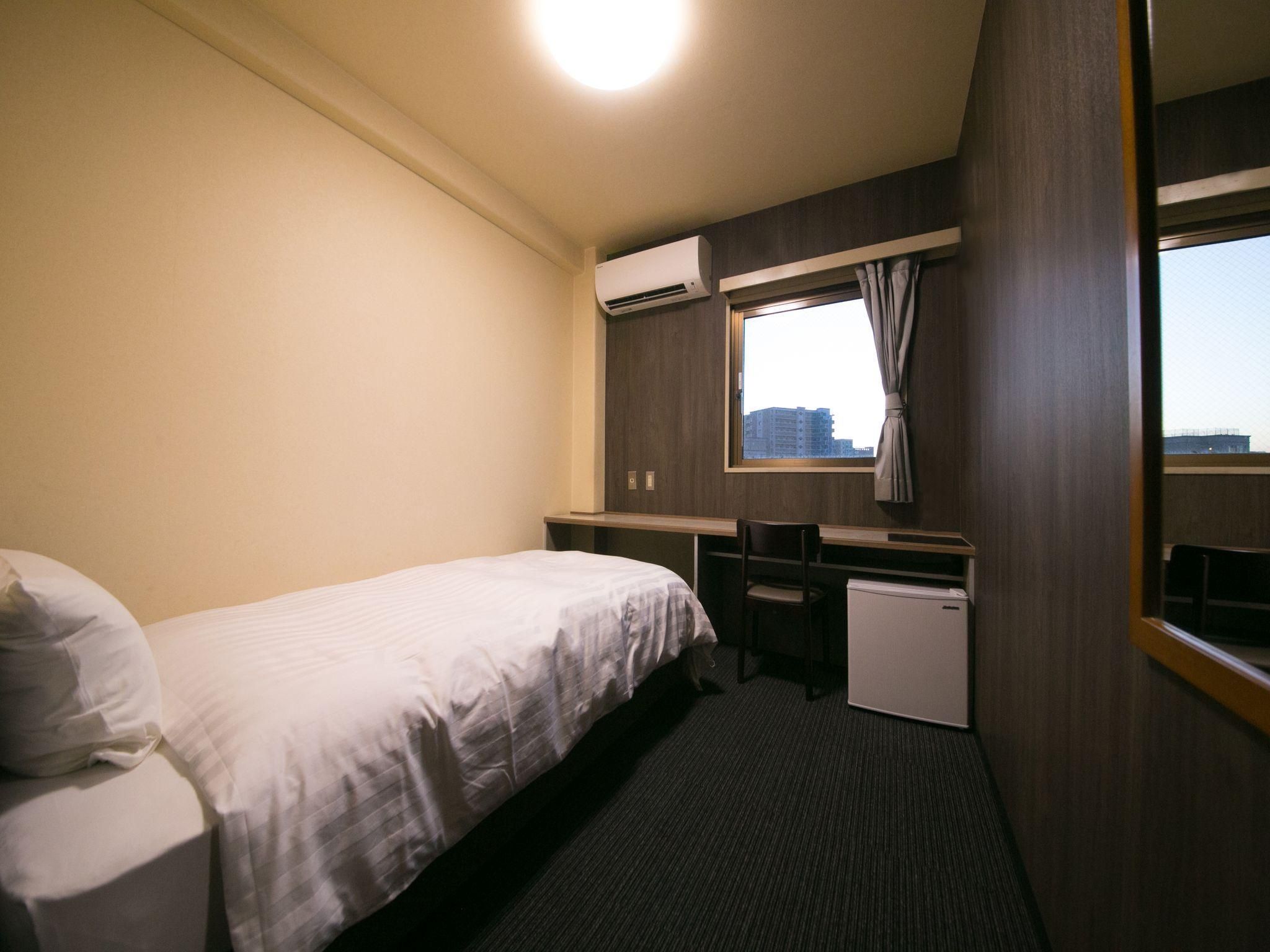 A hotel room with a bed, desk, chair, air conditioning unit, and a window with a view.