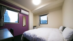 Ein Hotelzimmer mit Bett, Schreibtisch, Stuhl, Fenster und Klimaanlage.