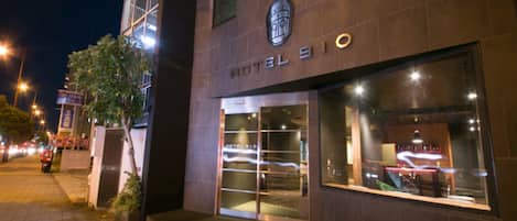 A hotel entrance with a modern facade, large glass windows, and a visible staircase leading to the entrance.