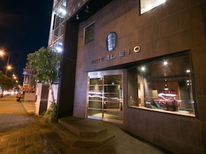 A hotel entrance with a modern facade, large glass windows, and a visible staircase leading to the entrance. - Hotel 910 (Oita)