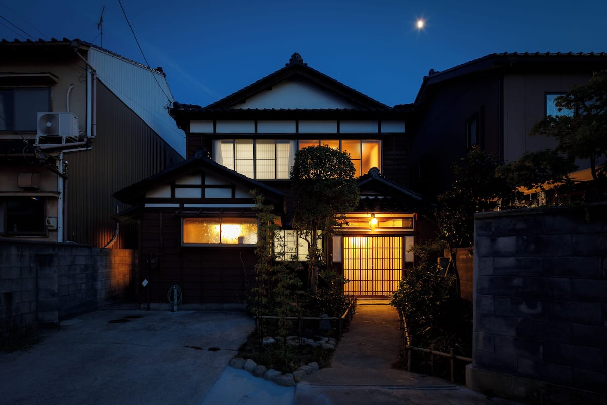 Ein traditionelles japanisches Haus im Dämmerlicht mit sichtbarem Eingang, einem kleinen Garten und einem klaren Nachthimmel.