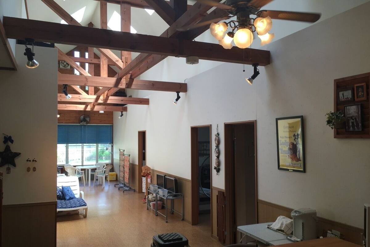 A spacious room with wooden beams, a ceiling fan, and a dining area with chairs and a table.