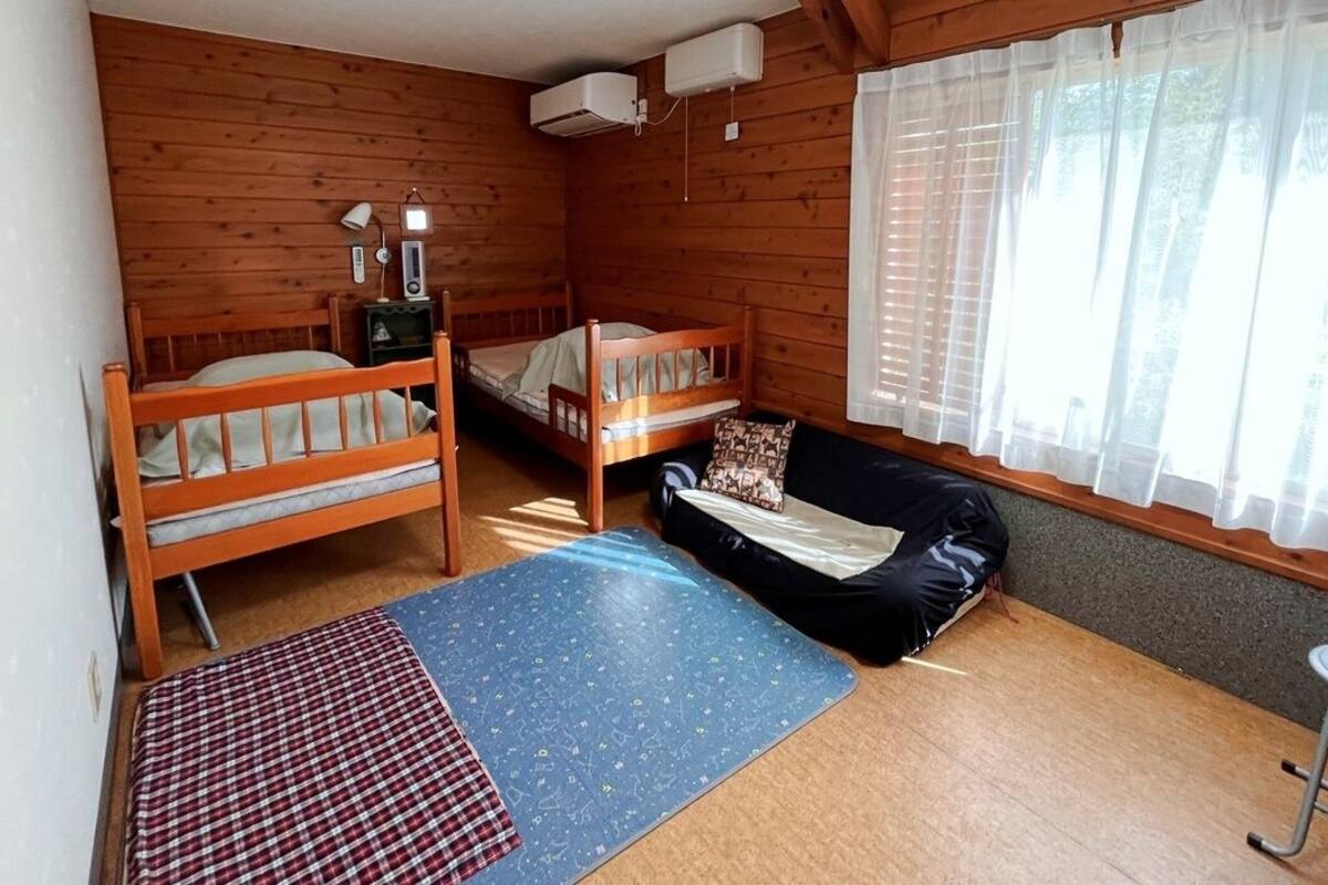 A cabin-style room with two wooden bunk beds, a sofa, a small table, and a window with curtains.